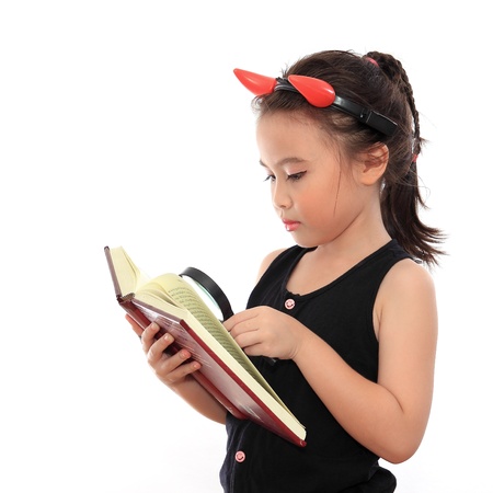 Beautiful little asian girl reading book with magnifying glassの写真素材