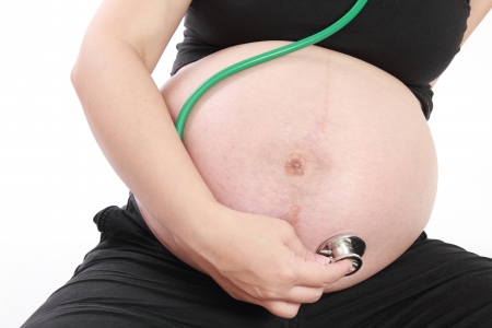 Pregnant woman examining belly with stethoscope isolated on white backgroundの写真素材