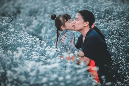 Mother kisses daughter in the flower gardenの写真素材