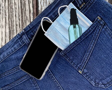 Medical face mask ,hand sanitizer spray in the blue jeans back pocket and a smartphone on table(new...