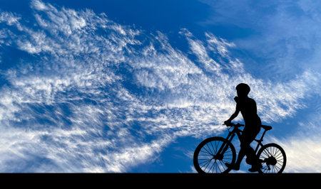Silhouette of young man riding on modern bike on the road with bright cloud sky background, Sport and active life concept in the summer ,の写真素材