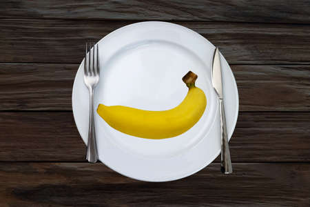 The fork and knife with fresh banana on the white plate . Table setting,の写真素材