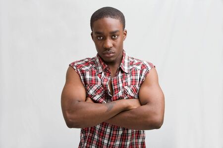 Young dark skinned handsome guy standing like a macho with both arms crossed wearing a checkerd shirt without sleeves.の写真素材