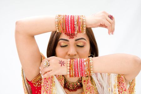 Beautiful face of a Bengali bride with her arms across her head covered with colorful bracelets and...