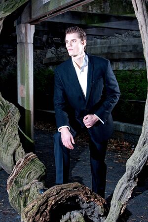 Handsome Caucasian guy having his foot on a vine tree under a pergola at night