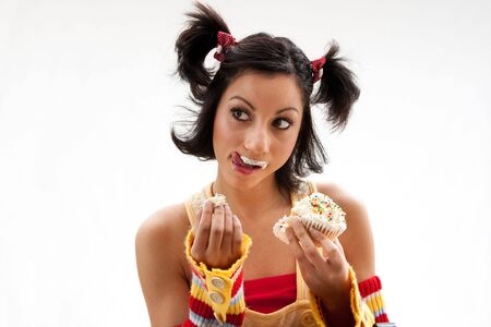 Beautiful Latina girl eating a cupcake with her fingers and licking her icing covered lip, isolatedの写真素材