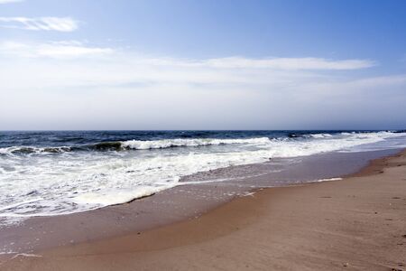 Beautiful beach with ocean sea crashing rolling waves under a blue sky with white clouds, rip currents.の写真素材