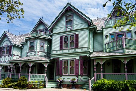 Beautiful big old nostalgic historic wooden green with purple Victorian house building with porch.の写真素材