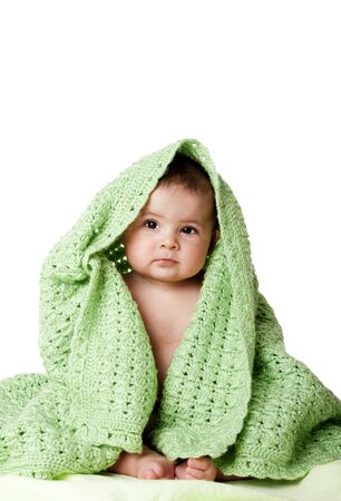 Beautiful cute innocent Caucasian Hispanic baby face while sitting and covered between green knitted blankets, isolated.の写真素材