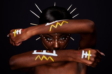 Beautiful cultural tribal African female face with arms and hands in fron, yellow, red and white makeup cosmetics lines dots, sticks in hair.の写真素材