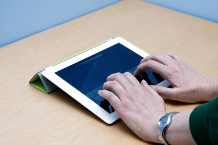 Female user hands typing on the new iPad 2 from Mac Apple, on a wooden desk and blue background.のeditorial素材