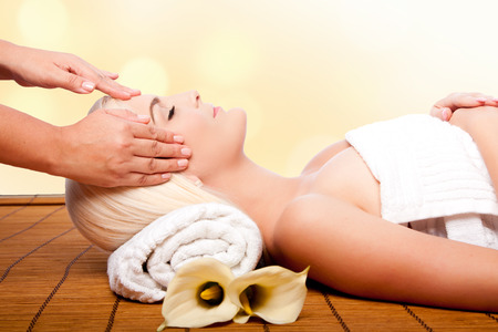 Beautiful young woman relaxing at spa getting therapeutic pampering forehead massage.の写真素材