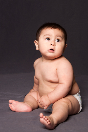 Cute happy funny baby sitting while wearing diaper, on gray.の写真素材