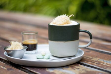 A cup of Hot Coffee with extra shot, sugar cotton candy and with thai traditional snacks on white plate, wood table natural backgroundの写真素材
