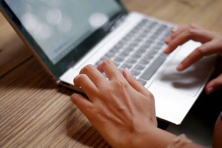 Woman's hand working on keyboard laptop computer on wood table in a cafe ,Blurred and soft focus imageの写真素材