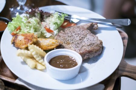 Grilled steaks and New Orleans Chicken Wings with vegetables  on a white plate on a wood tableの写真素材