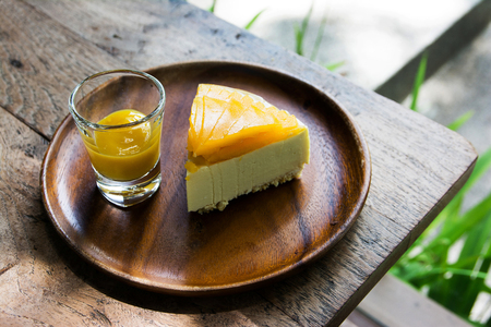 Mango fruit cake with mango cream sauce in glass on wooden plate backgroundの写真素材