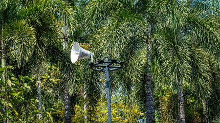 Horn speaker on metal pole in the park. White megaphone on steel post in the garden background.