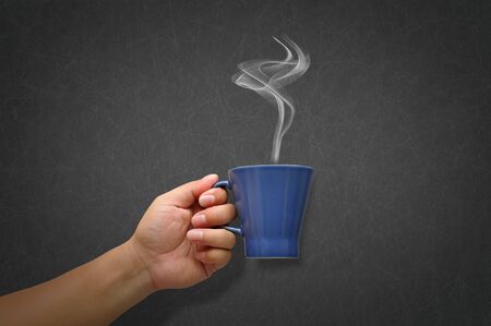 Hand holding a cup of coffee with white smokeの写真素材