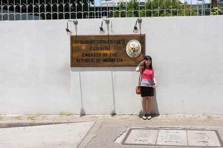 Bangkok, Thailand - June 28, 2015: Female tourist making salute gesture while taking a photograph with The Indonesia Embassy sign on sidewalkのeditorial素材