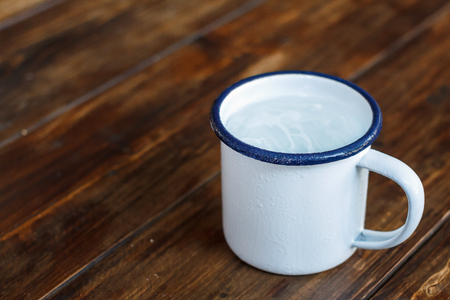 Mug of cool water with ice on wood table. Soft focus.の写真素材