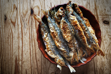 fried fish lying in a clay pot on a wooden tableの写真素材