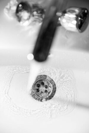 A stream of clean water flows into the drain hole of a white sink with a shallow depth of fieldの写真素材