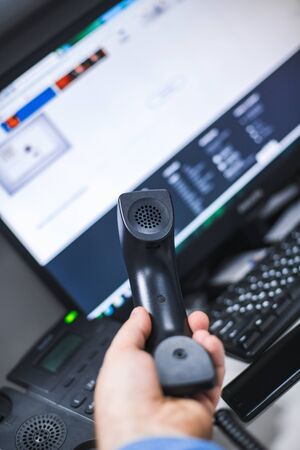 handset in hand and telephone with monitor and computer keyboard at shallow depth of fieldの写真素材