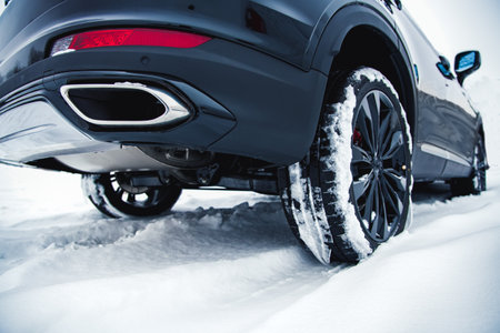 Car with winter tires on light-alloy wheels on snow at shallow depth of field