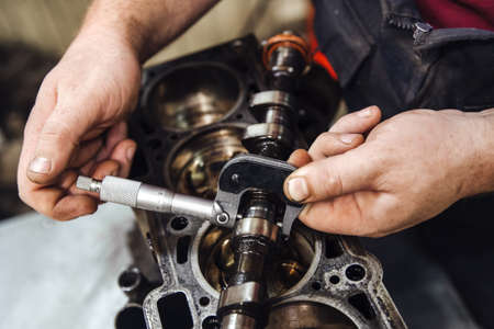 a measuring device in hand measures the camshaft against the background of a car engine at a shallow...