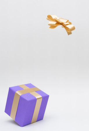 Golden ribbon in the air above blur purple gift box on white background .concept for happy surpriseの写真素材
