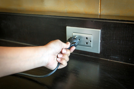 hand inserting an electrical plug into a wall socket.の写真素材