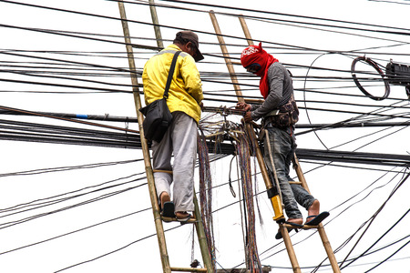 worker on bamboo ladder is repairing telephone line