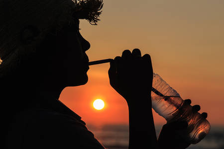 Silhouette of Thai woman drinking water at the beach in sunset timeの写真素材