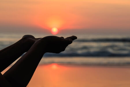 Silhouette of hands play with the sun at neach in sunset timeの写真素材