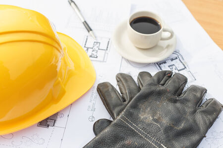 Close up work black glove with coffee, safety helmet and floor plan drawings on the tableの写真素材