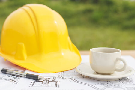Close up coffee cup and Yellow safety helmet with floor plan drawings on the table