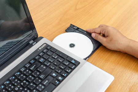 Hand inserting a cd on laptop on tableの写真素材