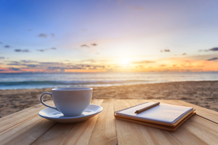 Close up coffee cup on wood table at sunset or sunrise beach