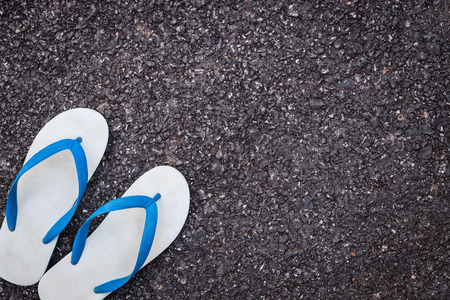 Pair of white plastic flip flop shoe on black asphalt roadの写真素材