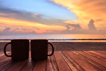 Close up coffee cup on wood table at sunset or sunrise beachの写真素材