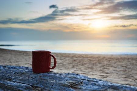 Close up coffee cup on wood log at sunset or sunrise beachの写真素材
