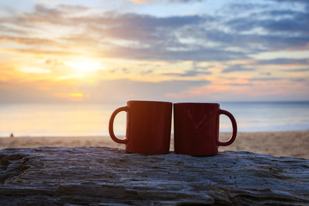 Close up coffee cup on wood log at sunset or sunrise beachの写真素材