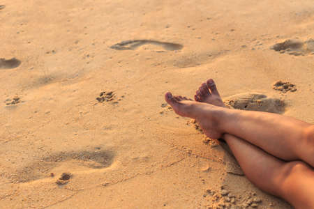 Legs of woman sit on the beach at sunset timeの写真素材