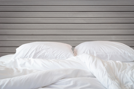 Close up white bedding sheets and pillow on wooden wall room background, Messy bed concept