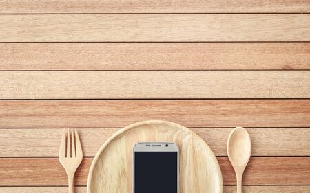 Top view smartphone on wooden dish on wooden plank background, concept Eating technologyの写真素材
