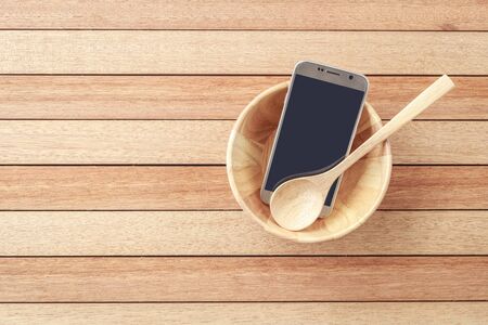 Top view smartphone in wooden bowl on wooden plank background, concept Eating technologyの写真素材