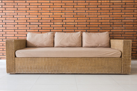 Rattan sofa with grey cushions and red brick wall background