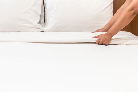 Close up hand set up white bed sheet in hotel roomの写真素材
