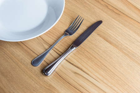 Close up fork and knife with white plate on wooden backgroundの写真素材